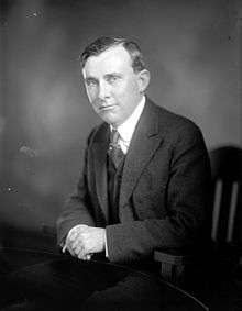 Black and white portrait of a man in a suit sitting in a chair.