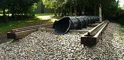 Exterior in woodland. a short section of railway line on wooden sleepers with a cast iron pipe of approximately one foot diameter, running inline with the rails