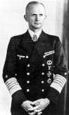 Black-and-white portrait of a man wearing a navy uniform displaying various military decorations and a neck order in shape of an Iron Cross, his hair is combed back.