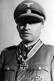 A man wearing a military uniform and peaked cap with an Iron Cross displayed at the front of his uniform collar.