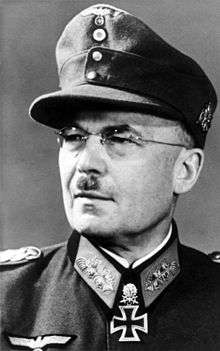 A black-and-white photograph of a man in semi profile wearing a military uniform, field cap, glasses and a neck order in shape of an Iron Cross.