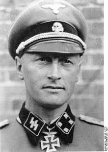 A man wearing a military uniform and peaked cap with an Iron Cross displayed at the front of his uniform collar.