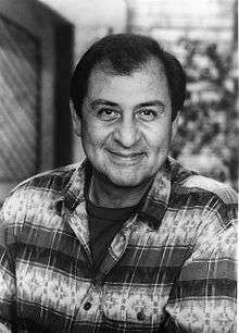 Handsome Latino man in his late sixties, smiling at the camera and wearing a striped shirt.