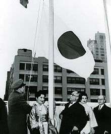 A group of men and women watching a flag being raised.