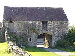 Stone building with archway through it for the road. Steps to wooden doorway on the first floor.