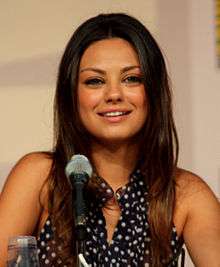 A woman with long brown hair, smiling into a microphone