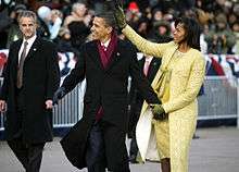 Barack and Michelle Obama acknowledge the crowd while the Secret Service and onlookers watch.