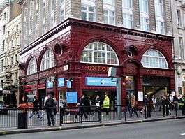 A red-bricked building with a sign reading "OXFORD CIRCUS HOUSE" in gold letters and a large number of people walking in the foreground