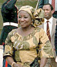 A woman in a yellow and green African-style dress smiles