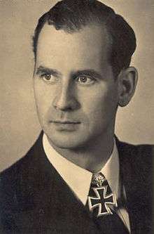 Black-and-white portrait of a man in semi profile wearing a military uniform with an Iron Cross displayed at his neck, his hair is combed back.