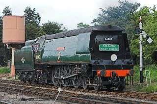 Side-and-front view of a large 4-6-2 steam locomotive with a tender. The locomotive boiler is hidden by a casing of flat metal side sheets.