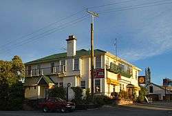 A two-storey, wooden pub, with Dominion Breweries signage. A telephone pole and a small utility vehicle are in the foreground.