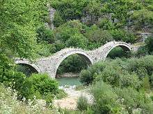 A three arched stone bridge stands over a small torrent.